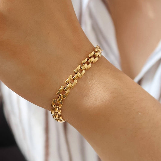 Gold chain bracelet on a wrist with a blurred white background