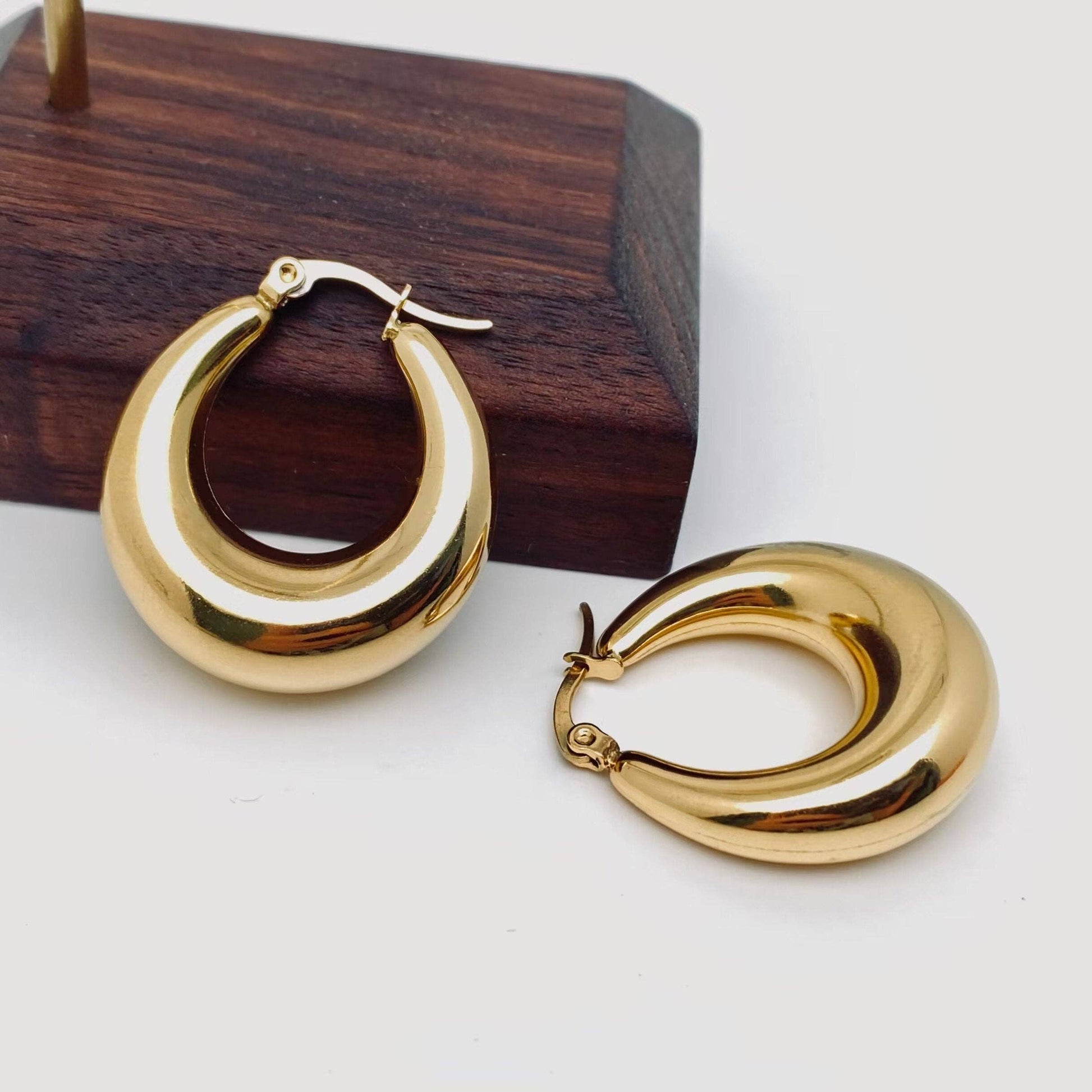 Glovia Jewels Gold hoop earrings on a white surface with a wooden block in the background