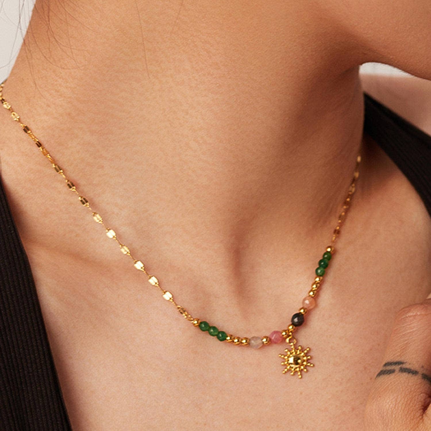 Gold necklace with green and red beads and a sun pendant on a person's neck.