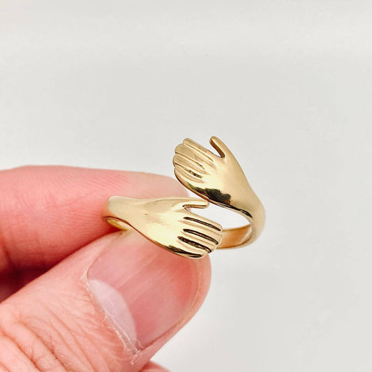 Gold hand-shaped ring held by a hand on a light gray background