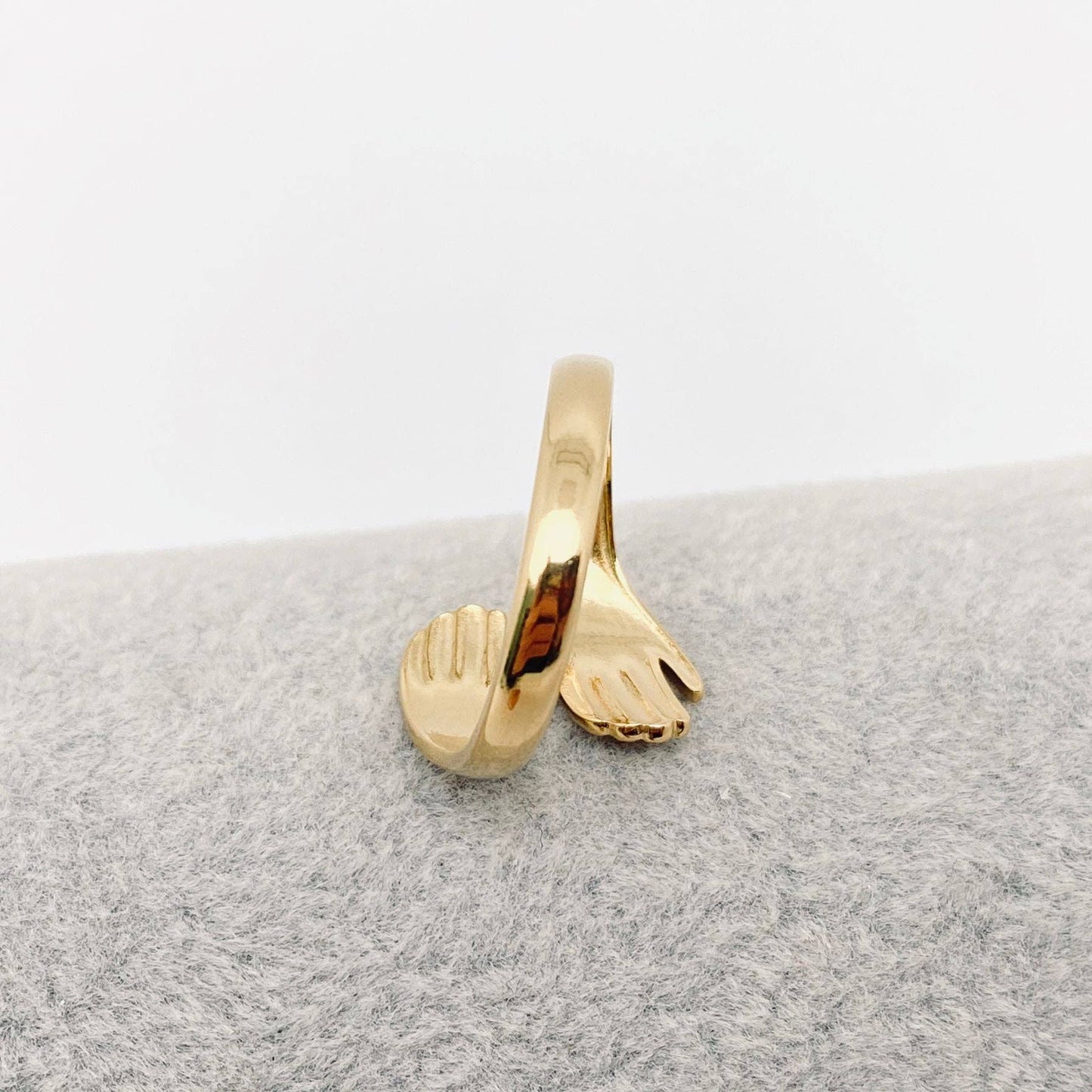Gold ring with hand and foot design on a gray cushion
